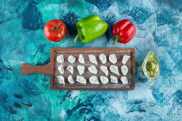 Oil and vegetables next to Turkish ravioli on a board , on the blue table. 