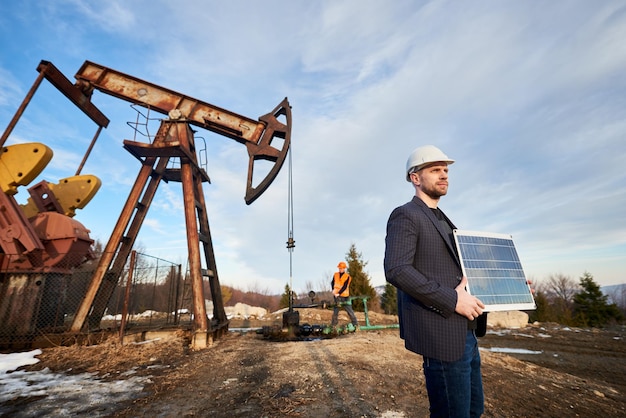 Oil worker in helmet holding solar panel