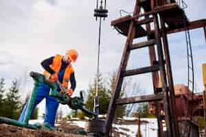 Free photo oil worker in orange uniform and helmet working with a pipe wrench near an oil pump jack