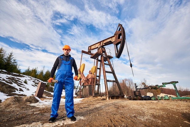 Free photo oil worker in uniform and helmet working in an oilfield next to a pump jack on a sunny day