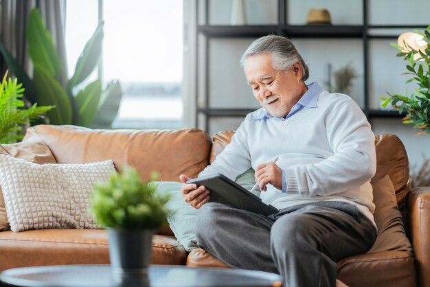 Old asian senior grandfather enjoy sunday weekend reading notebook on sofa couch at homehome isolation senior male adult relax casual happiness at home