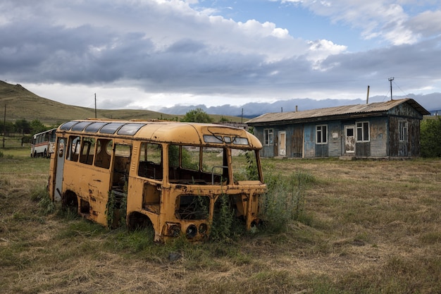 Old broken bus on a field by a house captured in Armenia