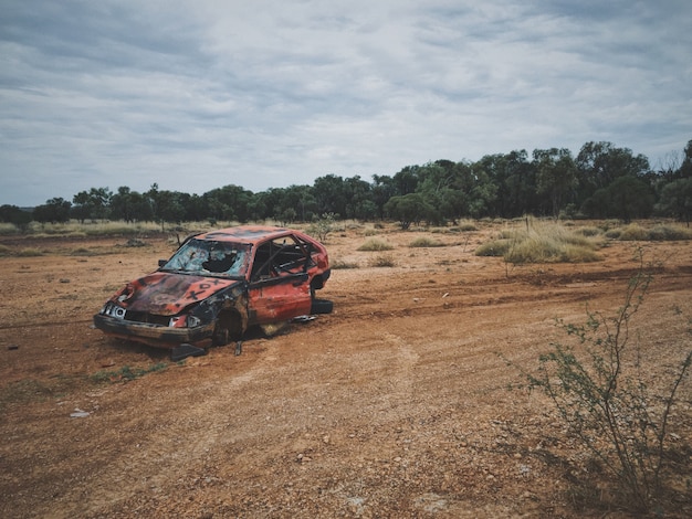 Free photo old broken up car in a dry grass field with trees