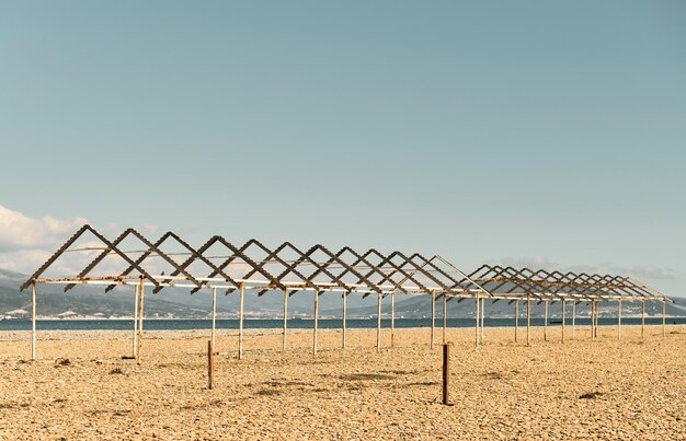 Old canopies from sun on a city pebble beach Black Sea coast empty calm beach on a sunny day The sky is burnt out at noon sea bay and in background is Caucasus mountains Calming pastel swatches