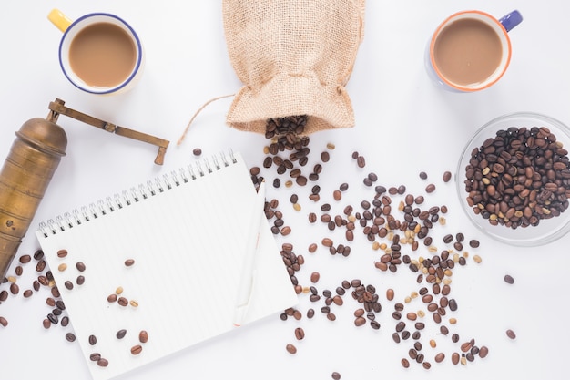 Free Photo old coffee grinder; coffee beans; coffee cup; blank spiral notepad with pen on white background