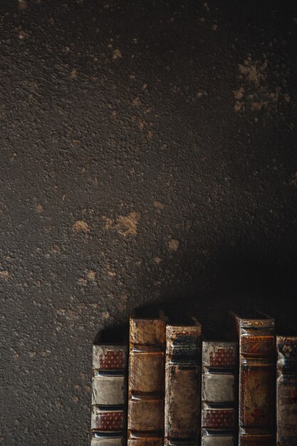 Old fashioned flat lay with stack of antique leather bound books against a dark wall. Literature, reading, education concept. Retro, vintage style. Copyspace for your ad. Antique archive.