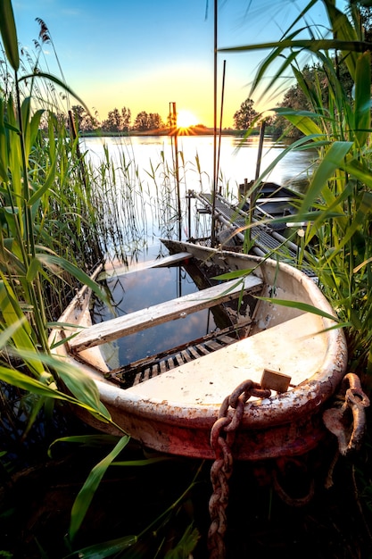 Old iron rowing boat partially sunk on the waterfront of a pond at sunset