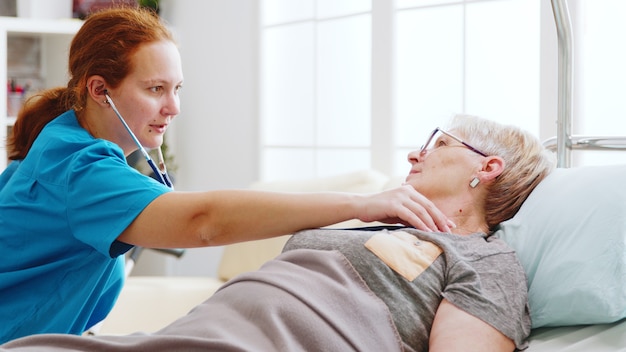 Free photo old lady getting her heartbeats checked by a female nurse in bright and cozy nursing home