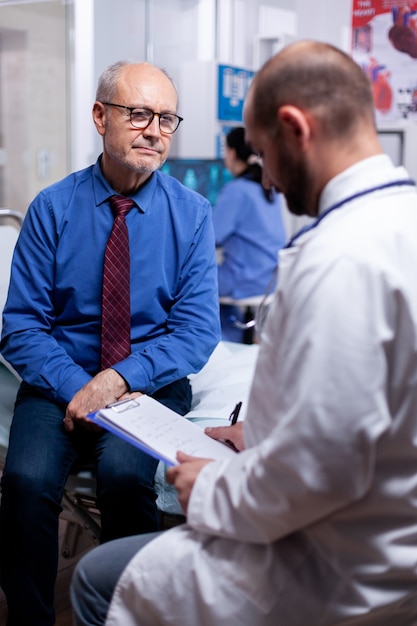 Free photo old man answering doctor questionnaire during examination in hospital room