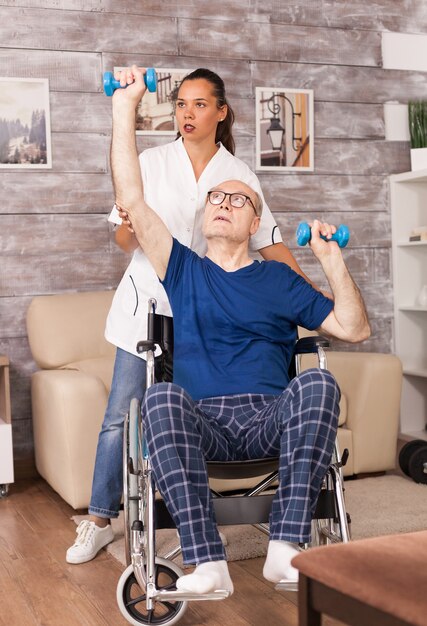 Old man doing exercises during rehabilitation helped by medical worker