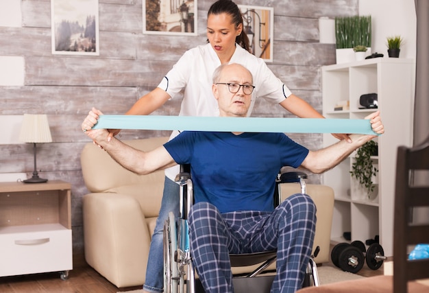 Old man doing muscle injury exercise using resistance band with nurse beside