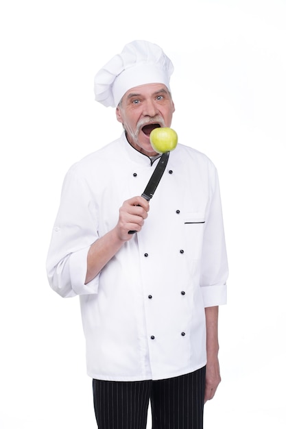 Free photo old man, professional chef in white uniform holding metal knife with green apple while staying on white wall