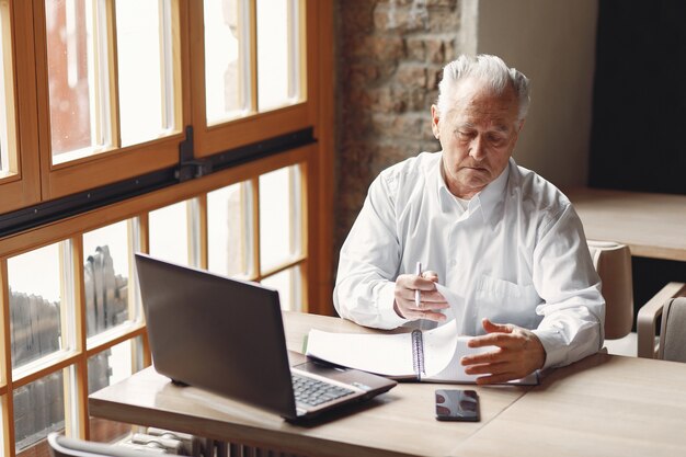 Old man sitting at the table and working with a laptop