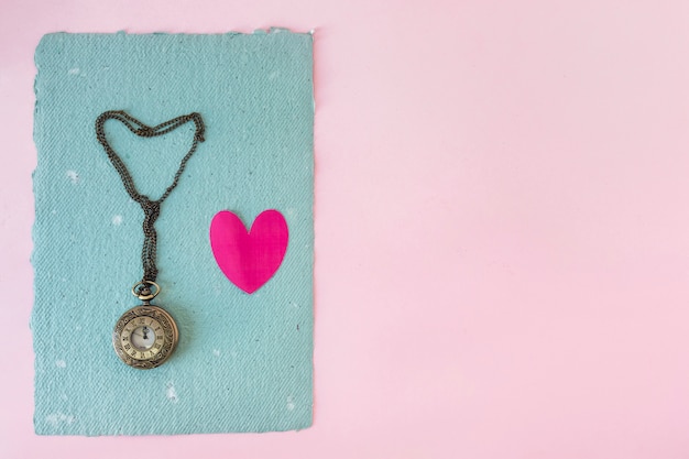 Old pocket watch and little heart on blue paper