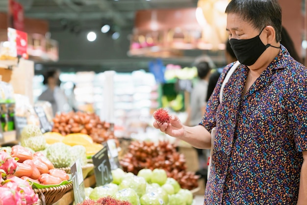 Free photo old senior asian woman wear virus spread protection mask while shopping fresh vagetable and fruit at grocery store in supermarket new normal lifestyle after lockdown is over