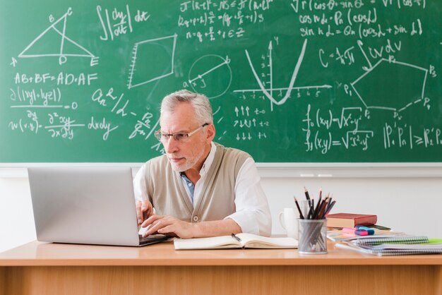 Old teacher using laptop in classroom