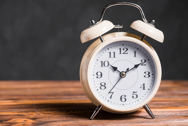 An old vintage alarm clock on wooden desk against black background