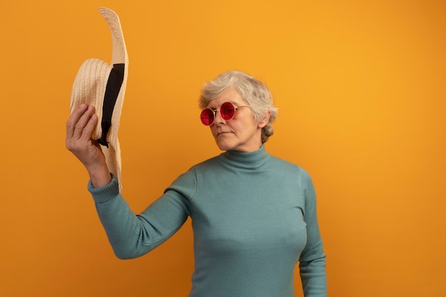 Free Photo old woman wearing blue turtleneck sweater and sunglasses holding and looking at hat 