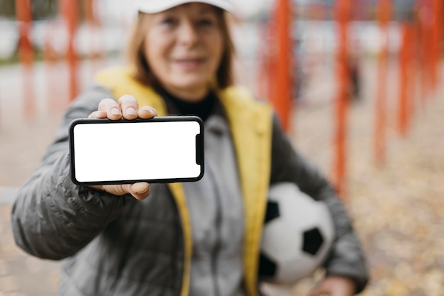 Free Photo older woman holding smartphone and football while working out outdoors