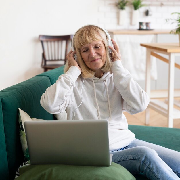 Older woman listening to music using headphones and laptop