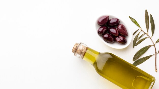 Olive oil bottle with leaves and purple olives with copy space