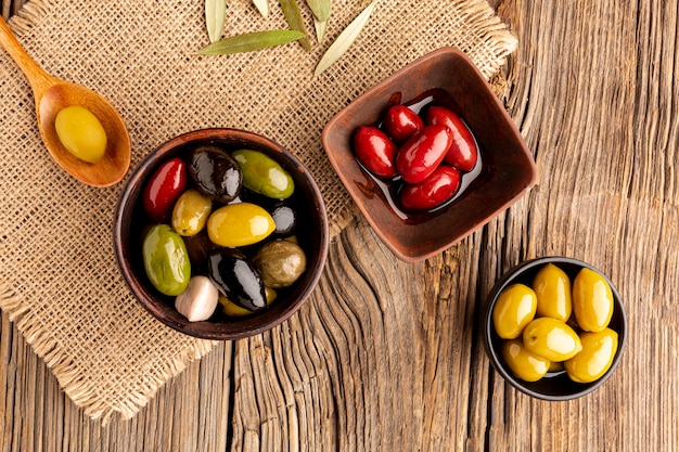 Olives in bowls and wooden spoon on textile material