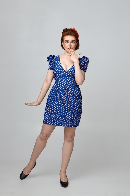 Free photo omg. astonished young beautiful housewife dressed in 60s retro outfit having naive amazed look, covering mouth, being shocked with unexpected news. pin up girl in vintage dress expressing shock