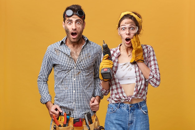 Free photo omg! wow! portrait of emotional surprised young european service technicians wearing safety goggles looking in full disbelief, keeping mouths wide opened and eyes popped out