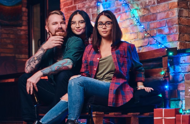 One bearded male and two brunette women Christmas party in a room with loft interior.