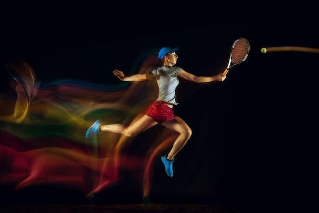 Free Photo one caucasian woman playing tennis isolated on black wall in mixed and stobe light. fit young female player in motion or action during sport game. concept of movement, sport, healthy lifestyle.