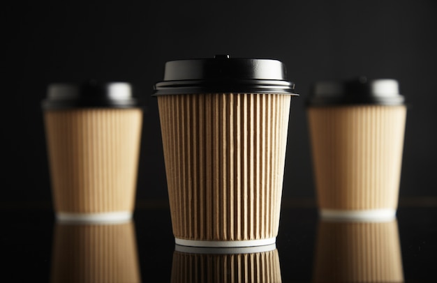 Free Photo one focused in front of unfocused brown take away cardboard paper cups closed with caps isolated on black and mirrored. retail  presentation