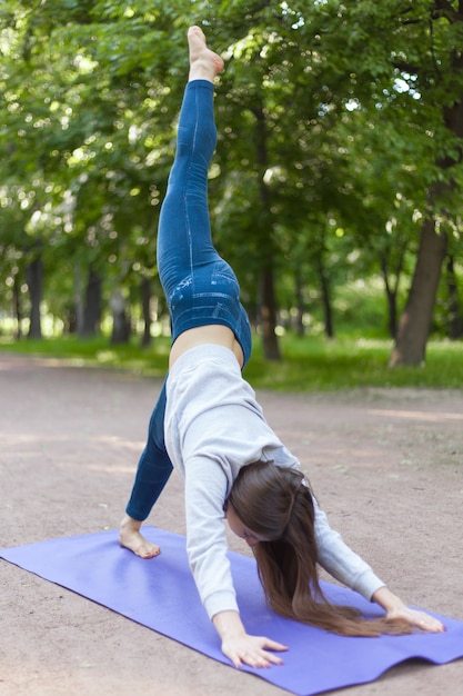 One-legged down dog yoga pose in park alley