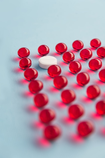 One white round tablet in a grid of red capsules