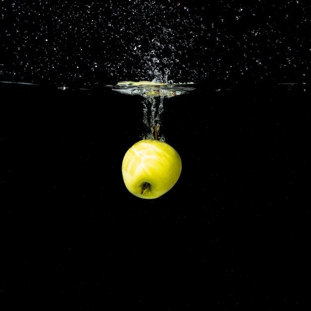 Free Photo one whole green apple splashing into water against black background