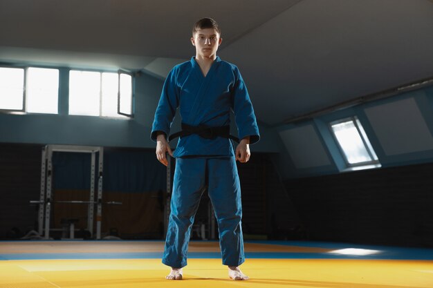 One young fighter in kimono training martial arts in the gym