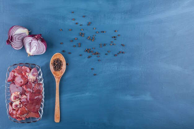 Onion, spoon, spice and offal in a bowl, on the blue background