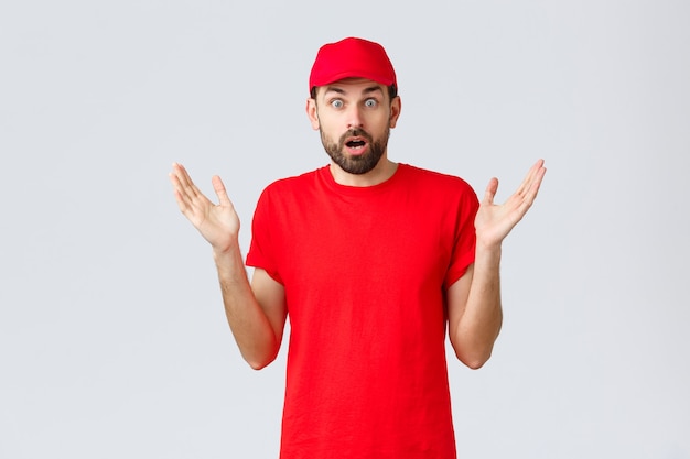 Free photo online shopping, delivery during quarantine and takeaway concept. confused and shocked courier in red t-shirt and cap of company service, raise hands up indecisive and nervous, cant believe smth