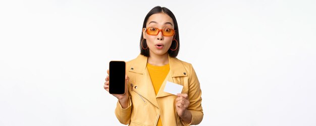 Online shopping and people concept stylish asian woman showing mobile phone screen and credit card s