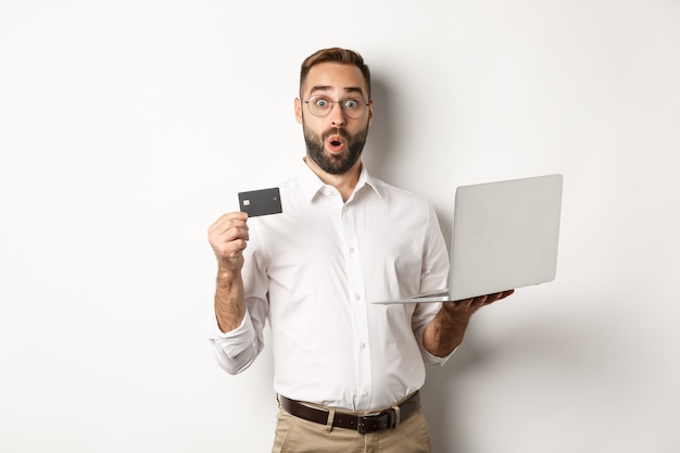 Online shopping. Surprised man holding laptop and credit card, shop internet store, standing  