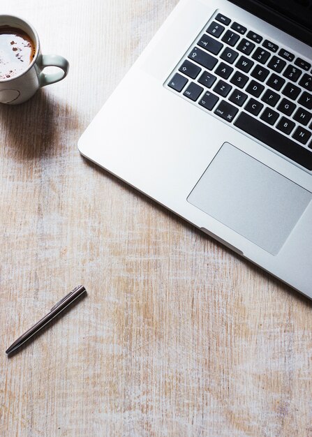 An open laptop with coffee cup and pen on wooden background