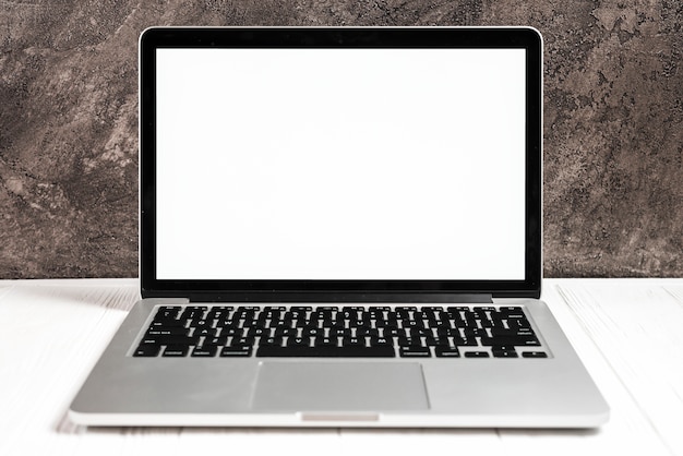 An open modern laptop with a white screen on white desk against concrete wall