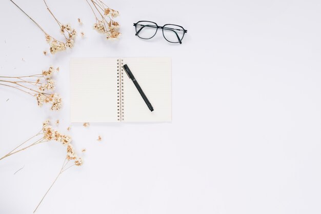 Open notebook; eyeglasses and flowers on white background