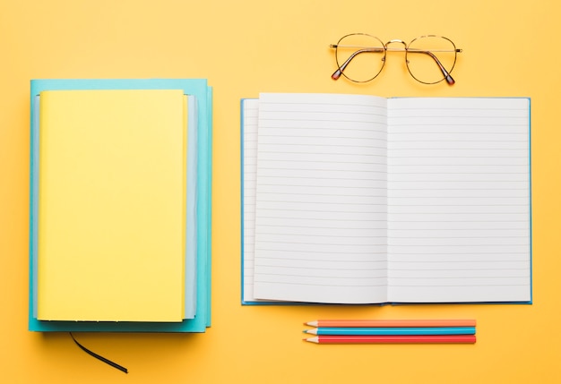 Free photo open notebook and stack of textbooks next to glasses and set of pencils