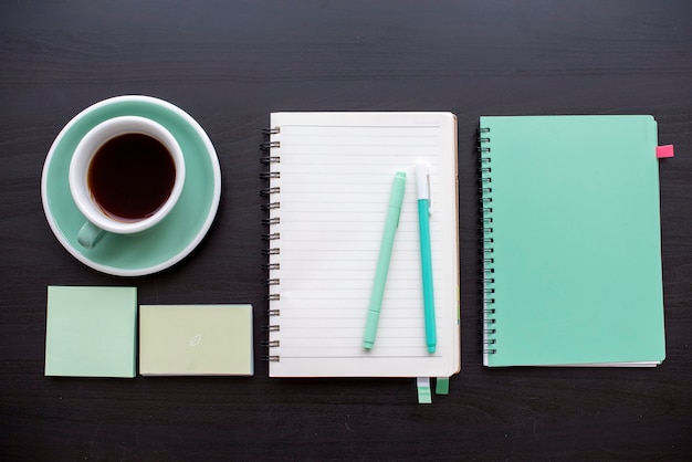 Open notebook with sticky note and pens stationery on dark gray table