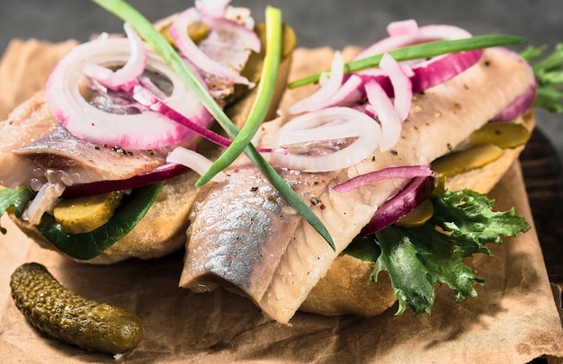 Free photo open sandwich with bread, pickled herring, pickled cucumber and red onion on a paper lining. danish smorebrod, selective focus and copy space