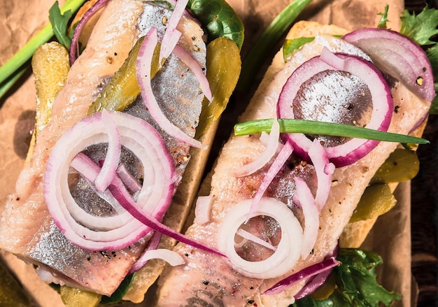 Free photo open sandwich with bread, pickled herring, pickled cucumber and red onion on a paper lining. danish smorebrod, selective focus and copy space