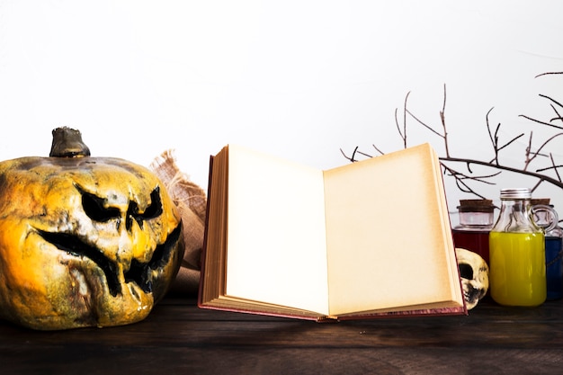 Opened book and spooky pumpkin on table