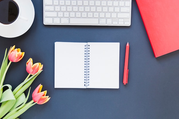 Opened notebook near coffee cup and keyboard on desk with tulip flowers