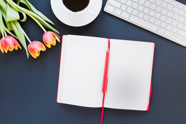 Opened notebook near coffee cup and tulip on desk with keyboard