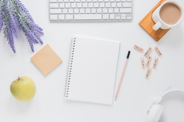 Opened notebook near stationery on white table with gadgets and coffee cup